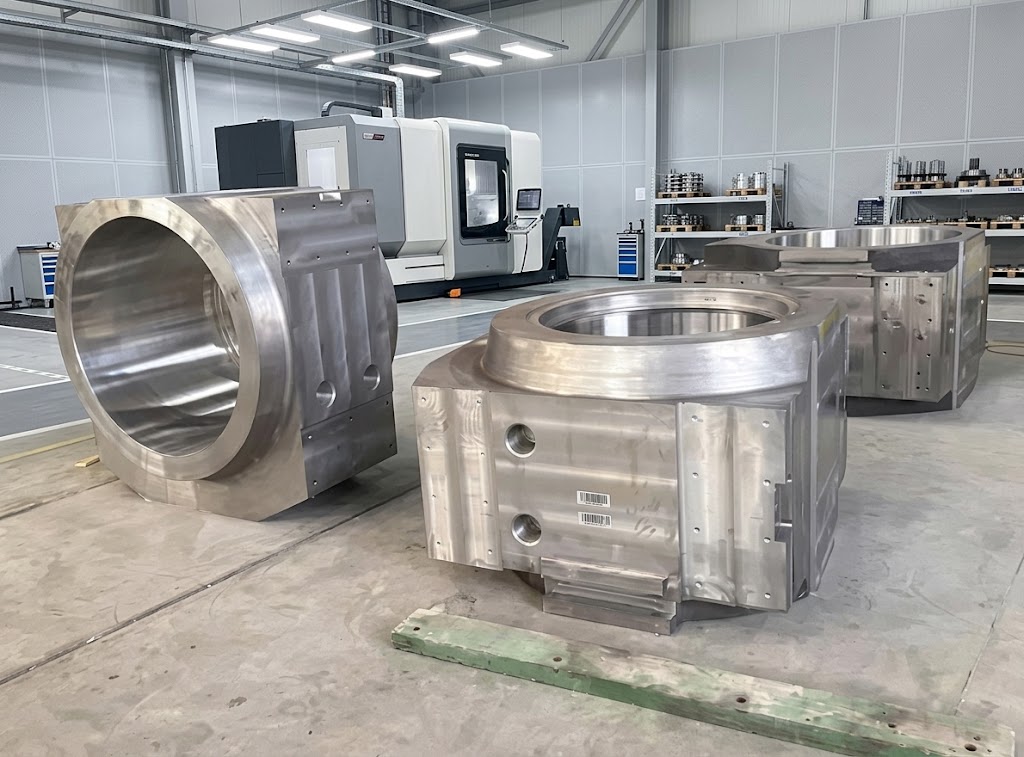 Close-up photograph of a large, freshly CNC-machined custom gray iron bearing housing sitting on a steel factory inspection table.