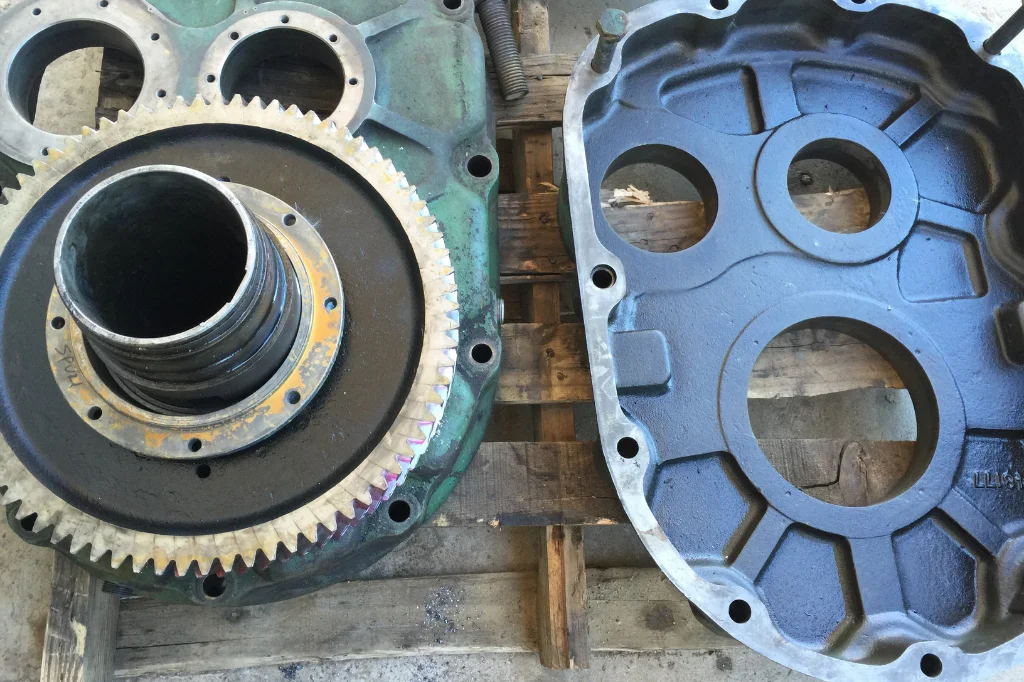 Close-up photograph of a heavy-duty custom sand-cast gray iron gearbox housing resting on a steel factory inspection table, showing precision CNC-machined bearing bores and a smooth internal finish, taken under bright overhead LED factory lighting